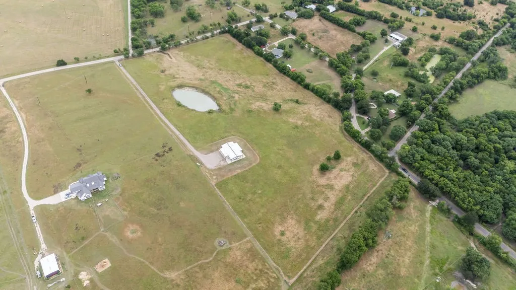 Expansive rural property featuring a primary residence with an asphalt driveway, a secondary structure, and a distinct pond