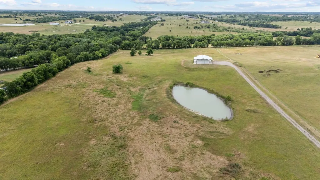 Expansive acreage featuring a private pond, a functional white barn, a long gravel driveway, and a perimeter of mature trees