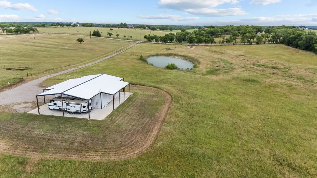 Expansive property featuring a large metal structure with a concrete pad, a gravel driveway, and a pond