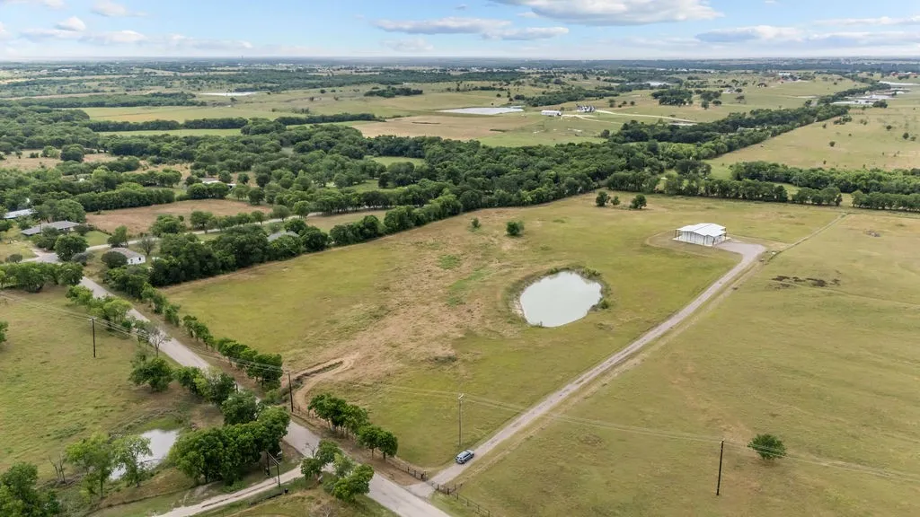Expansive rural landscape featuring a private pond, open fields, a long gravel driveway, and a large metal outbuilding