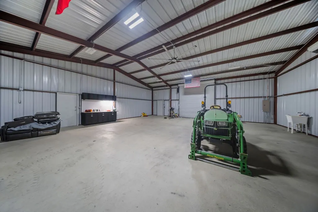 Spacious utility building featuring a concrete floor, high ceilings with exposed metal trusses, corrugated metal walls, and overhead lighting