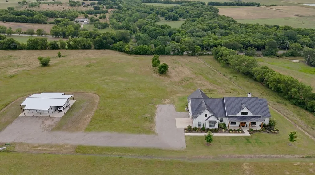 Contemporary farmhouse-style residence featuring a dark metal roof, light-colored exterior, and an expansive gravel driveway