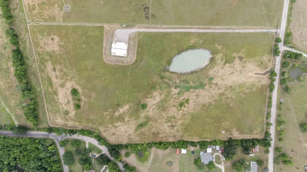 Expansive rural acreage featuring a natural pond, multiple paved roadways, and a prominent outbuilding