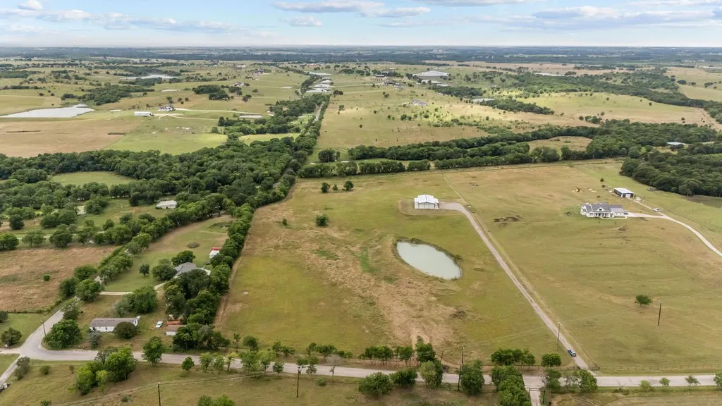 Expansive rural landscape featuring a private pond, multiple residential structures, wooded areas, and a network of unpaved roads
