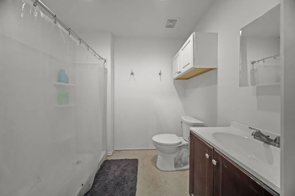 Full bathroom featuring a shower with built-in shelving, a single vanity with dark wood cabinetry, a white toilet, and an overhead medicine cabinet