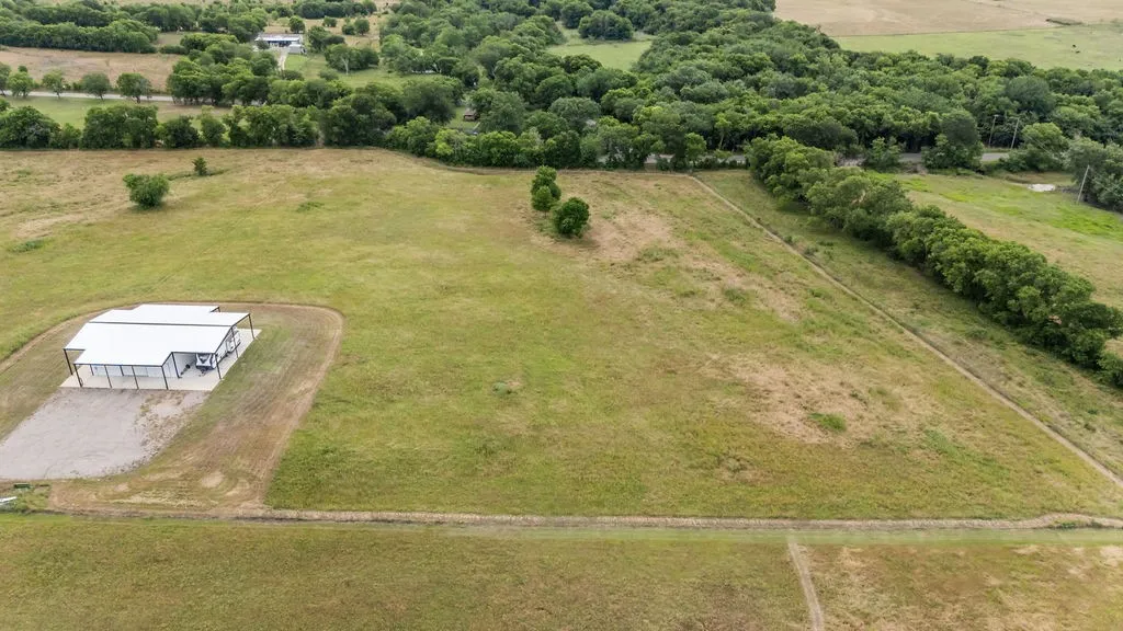 Expansive parcel featuring a modern metal-roofed structure with an extended covered patio, surrounded by open grassland and mature tree lines