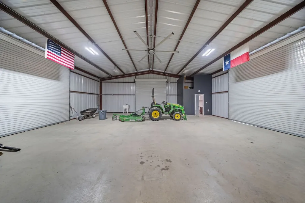 Spacious metal building with a high vaulted ceiling, exposed metal beams, concrete flooring, and multiple large roll-up doors