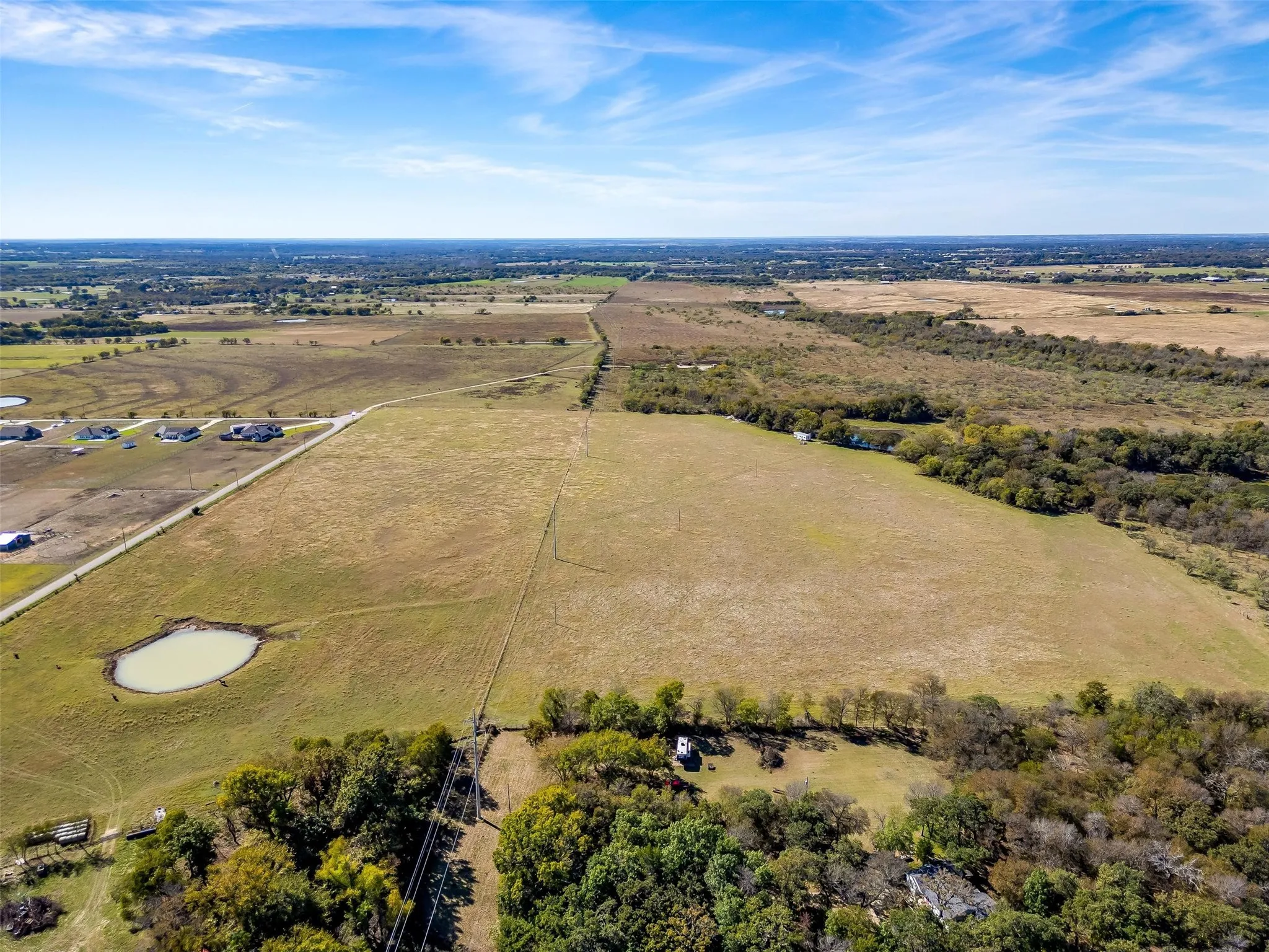 Expansive rural landscape featuring a prominent pond, mature trees, and open fields with defined property lines