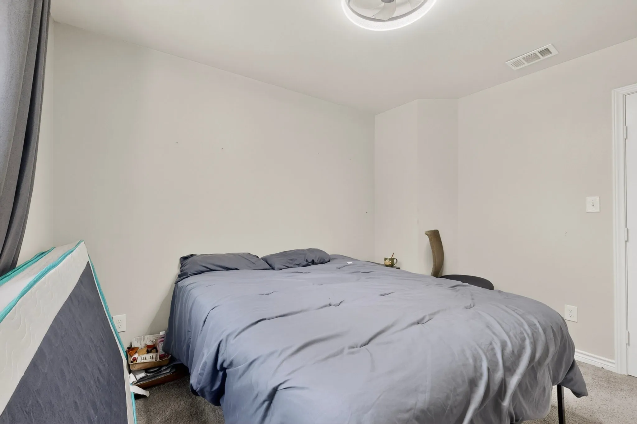Carpeted room featuring a ceiling fan with integrated lighting, wall-mounted air vent, and light-colored walls