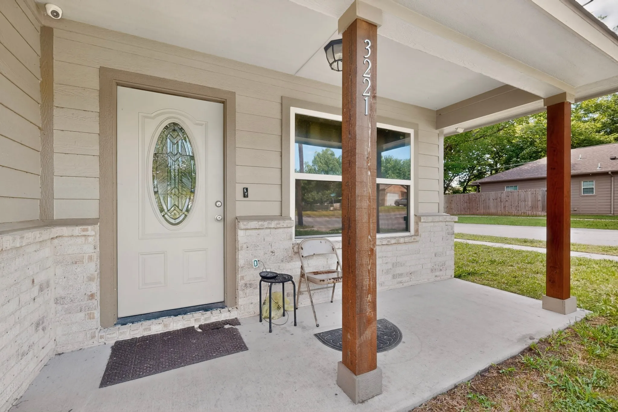 Covered front porch featuring wood-finish support columns, a white entry door with an oval stained-glass insert, and light-colored brick accents