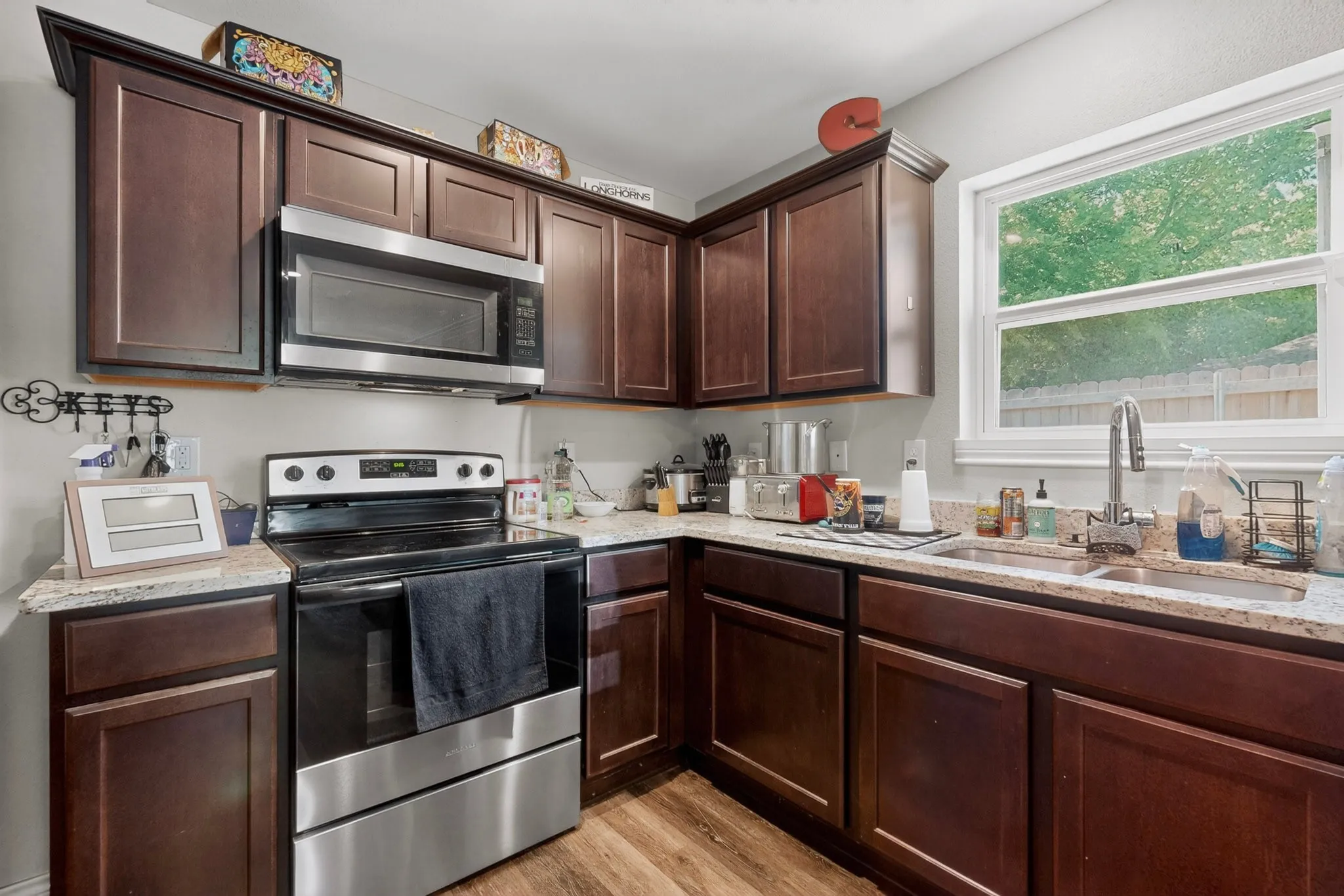 Kitchen featuring wood-finish cabinetry, light-toned countertops, a stainless steel over-the-range microwave, a stainless steel electric range, and a dual-basin stainless steel sink with a gooseneck faucet