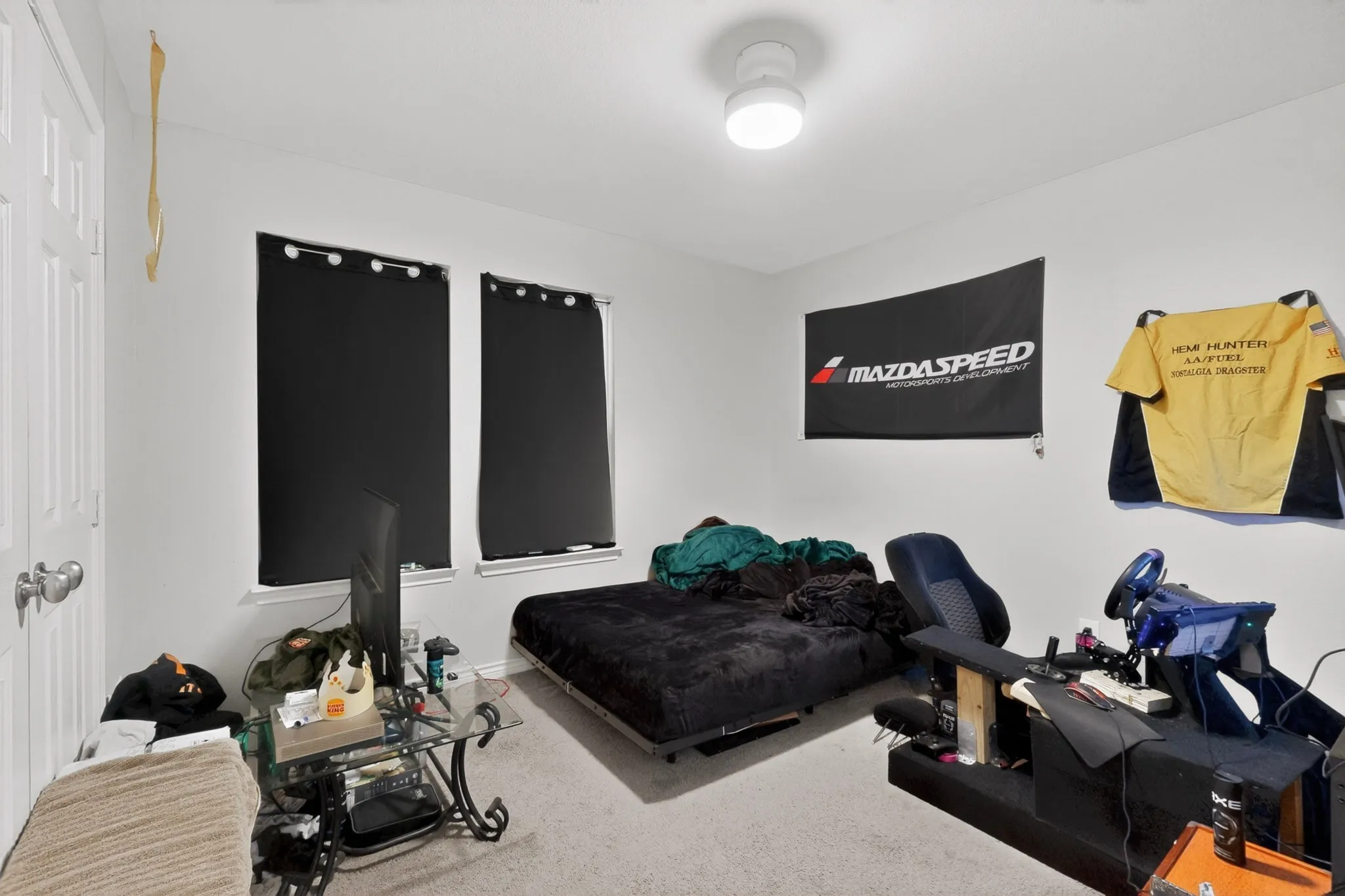 Room featuring light-colored walls, ceiling-mounted lighting, and two windows with black privacy coverings
