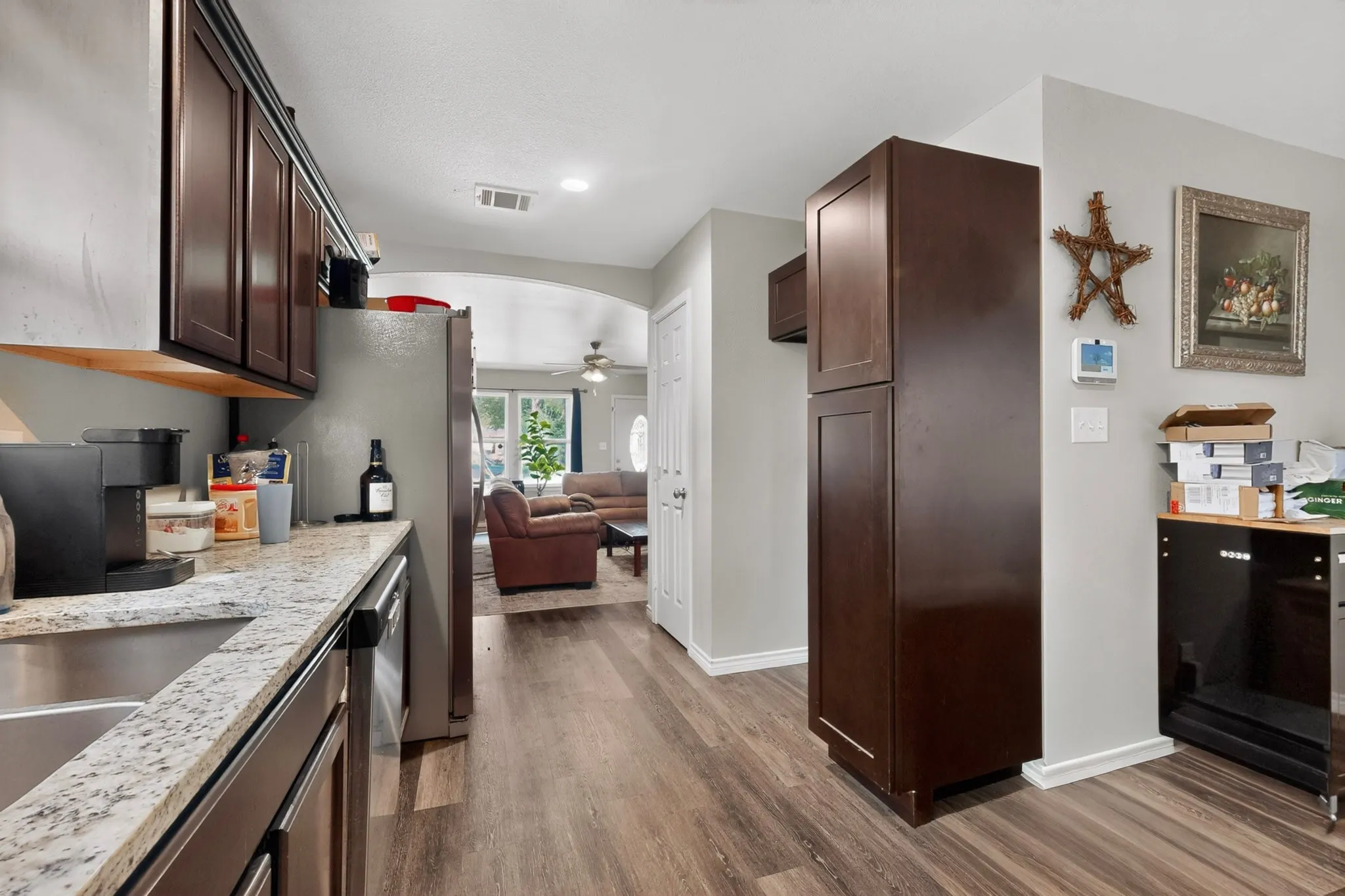 Kitchen featuring granite-look countertops, stainless steel sink, wood-finish flooring, dark wood cabinetry, and an arched entryway to another room