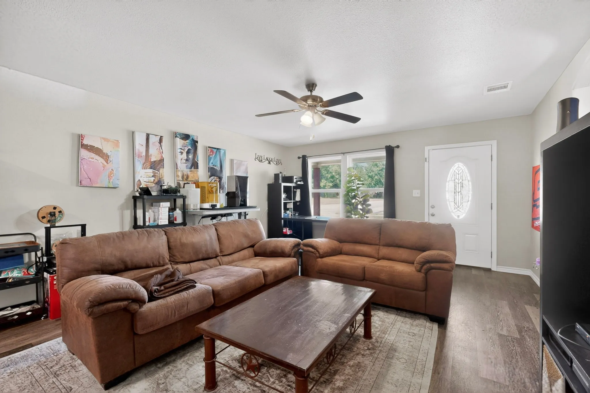 Spacious living area featuring wood-finish flooring, a ceiling fan, and ample natural light from a large window