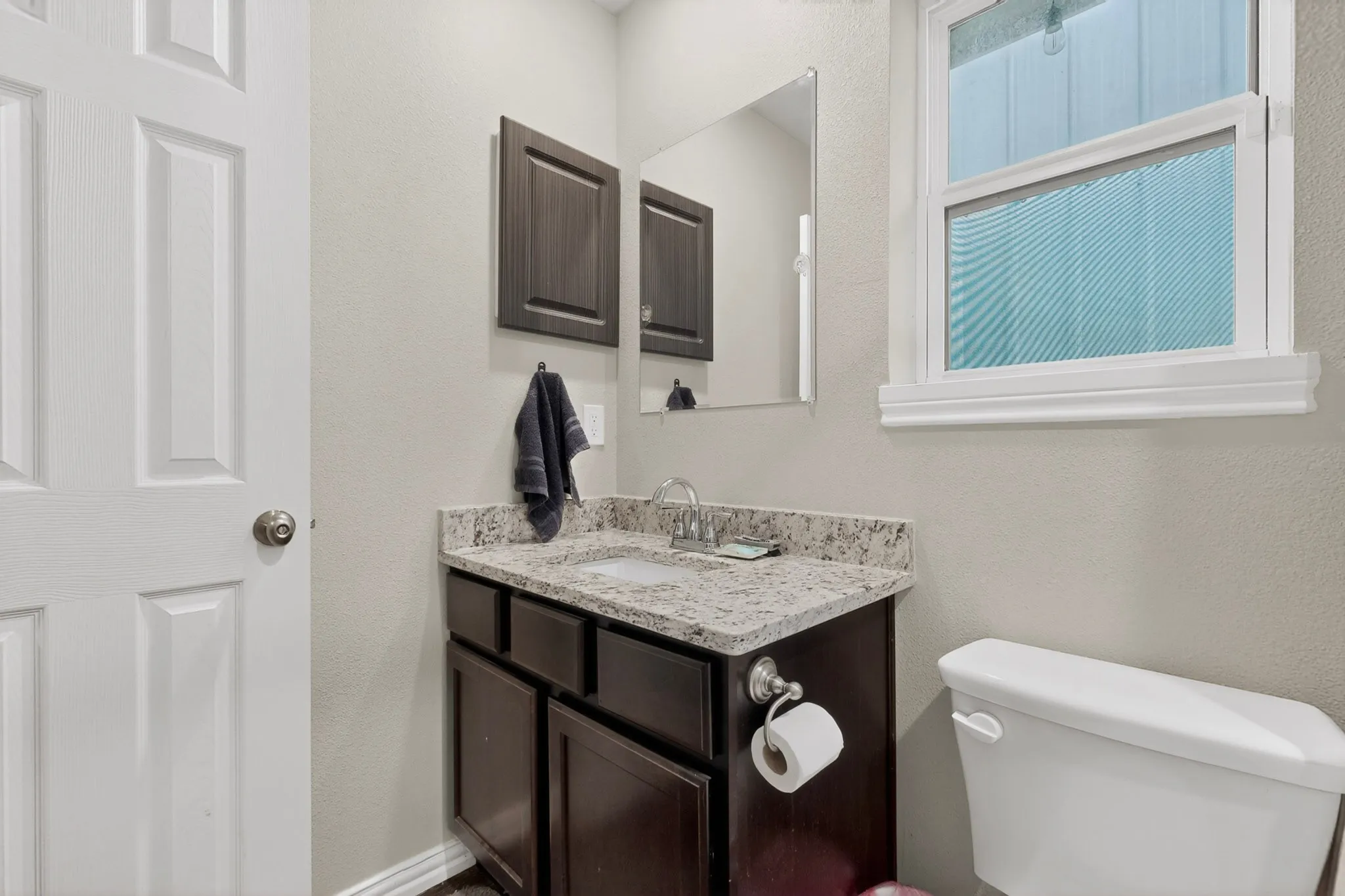 Powder room featuring a dark wood-finish vanity with a granite-style countertop, undermount sink, and modern faucet