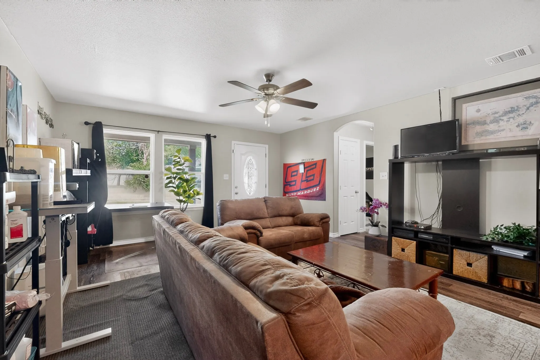 Living area featuring wood-finish flooring, light grey wall paint, white trim, and a ceiling fan with integrated lighting