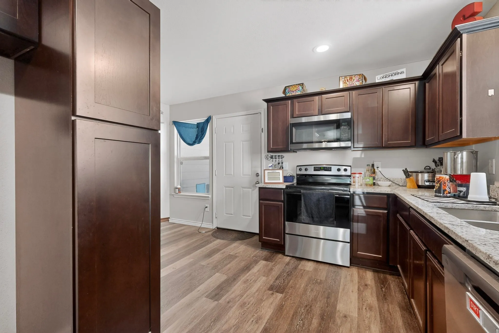 Kitchen featuring dark wood cabinetry, stainless steel appliances, light-toned granite countertops, and wood-finish flooring