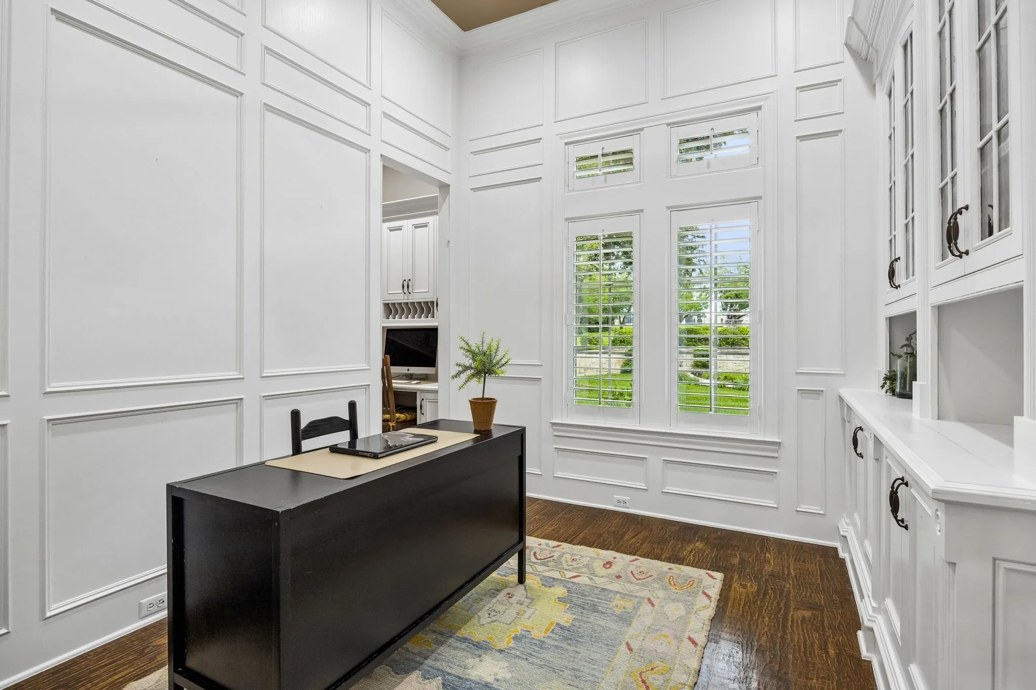 Dedicated room featuring extensive white paneling, wood-finish flooring, plantation shutters, and built-in cabinetry with glass-front doors