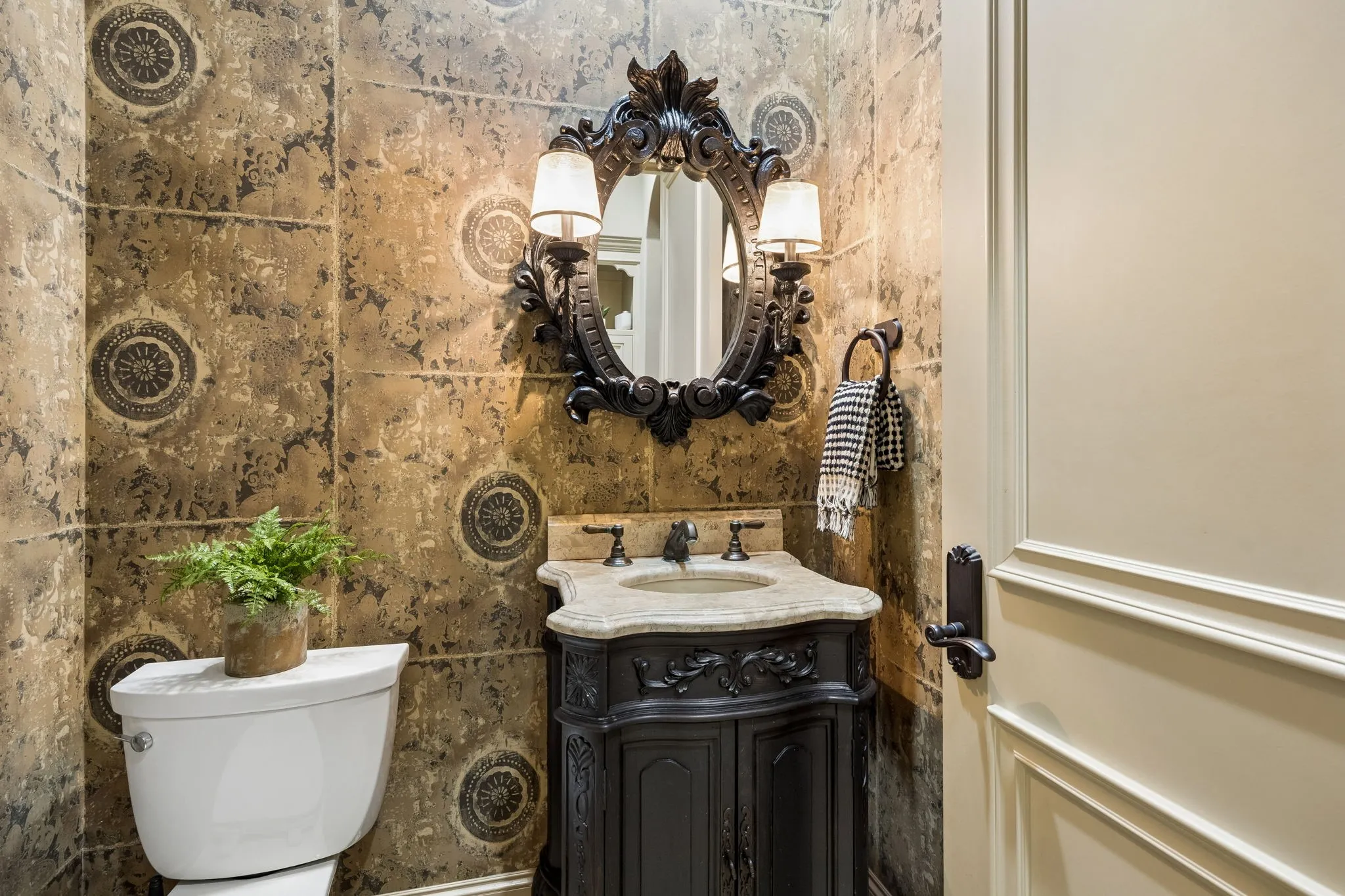 Powder room featuring decorative wall panels, a carved wood-finish vanity with a stone countertop, an ornate framed mirror, and a wall-mounted sconce