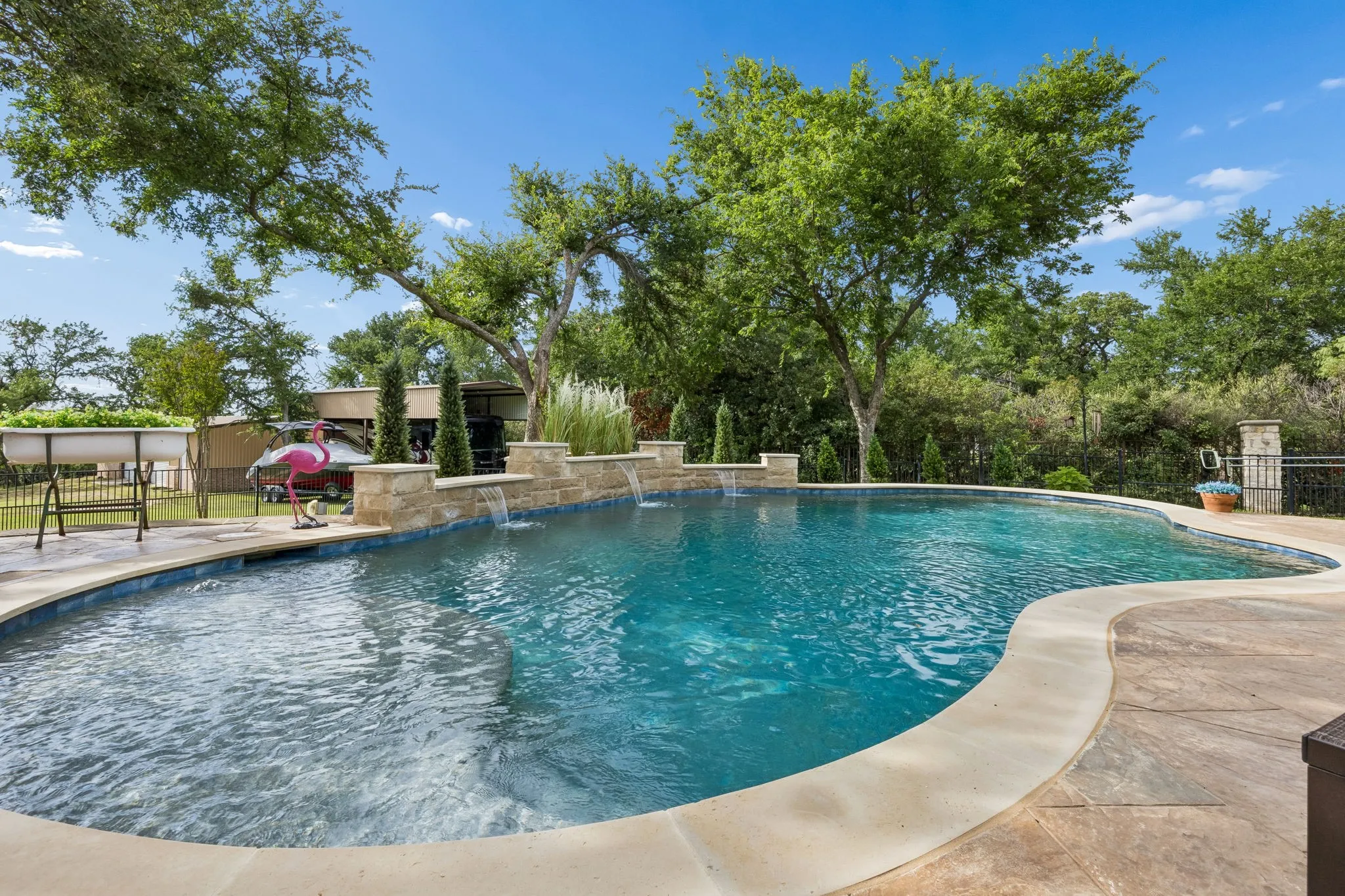 Freeform swimming pool with stone coping, stamped concrete surround, and integrated water features