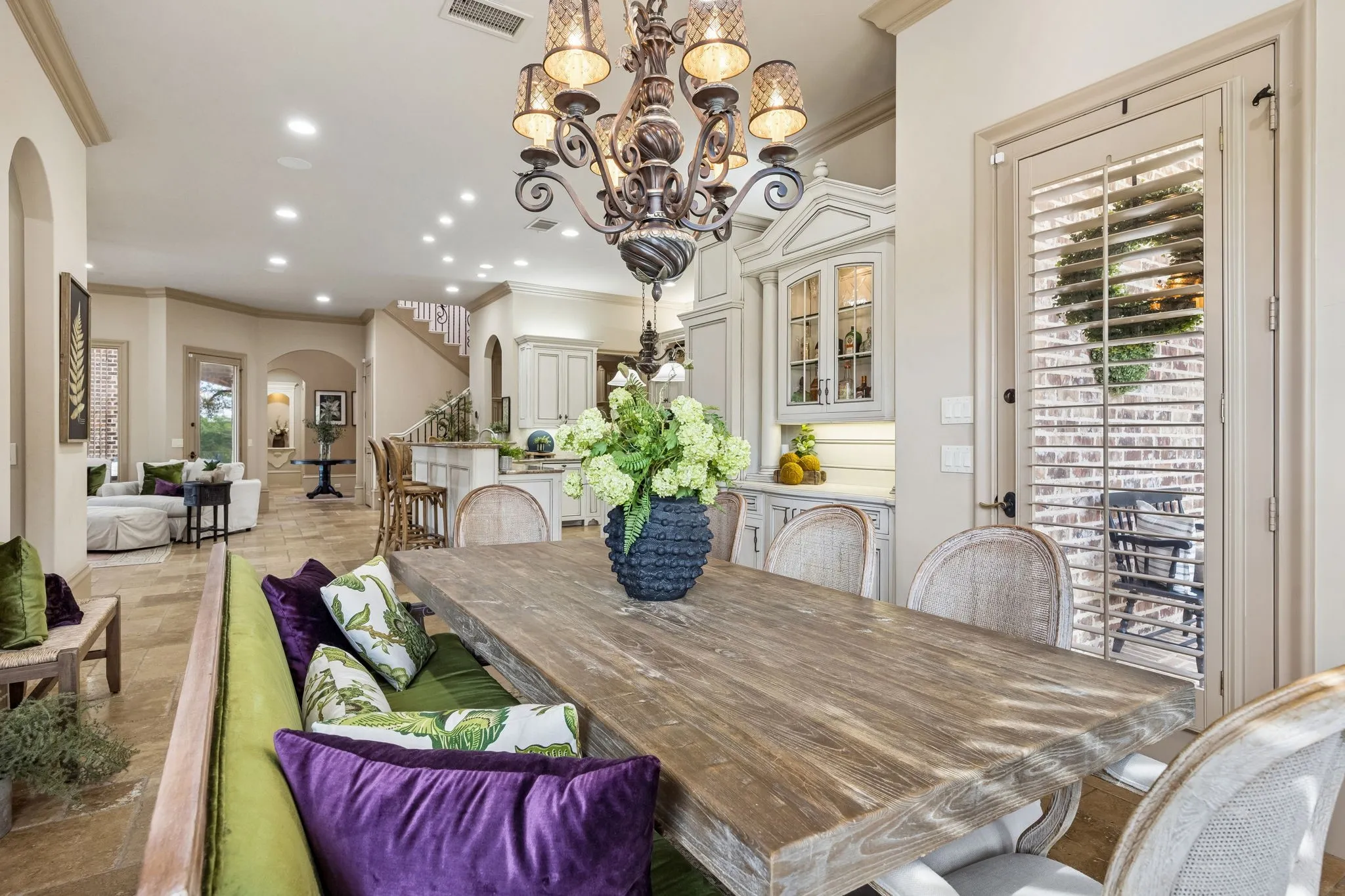 Dining area featuring a rustic wood table, an ornate chandelier, and direct access to an outdoor patio through a plantation-shuttered door