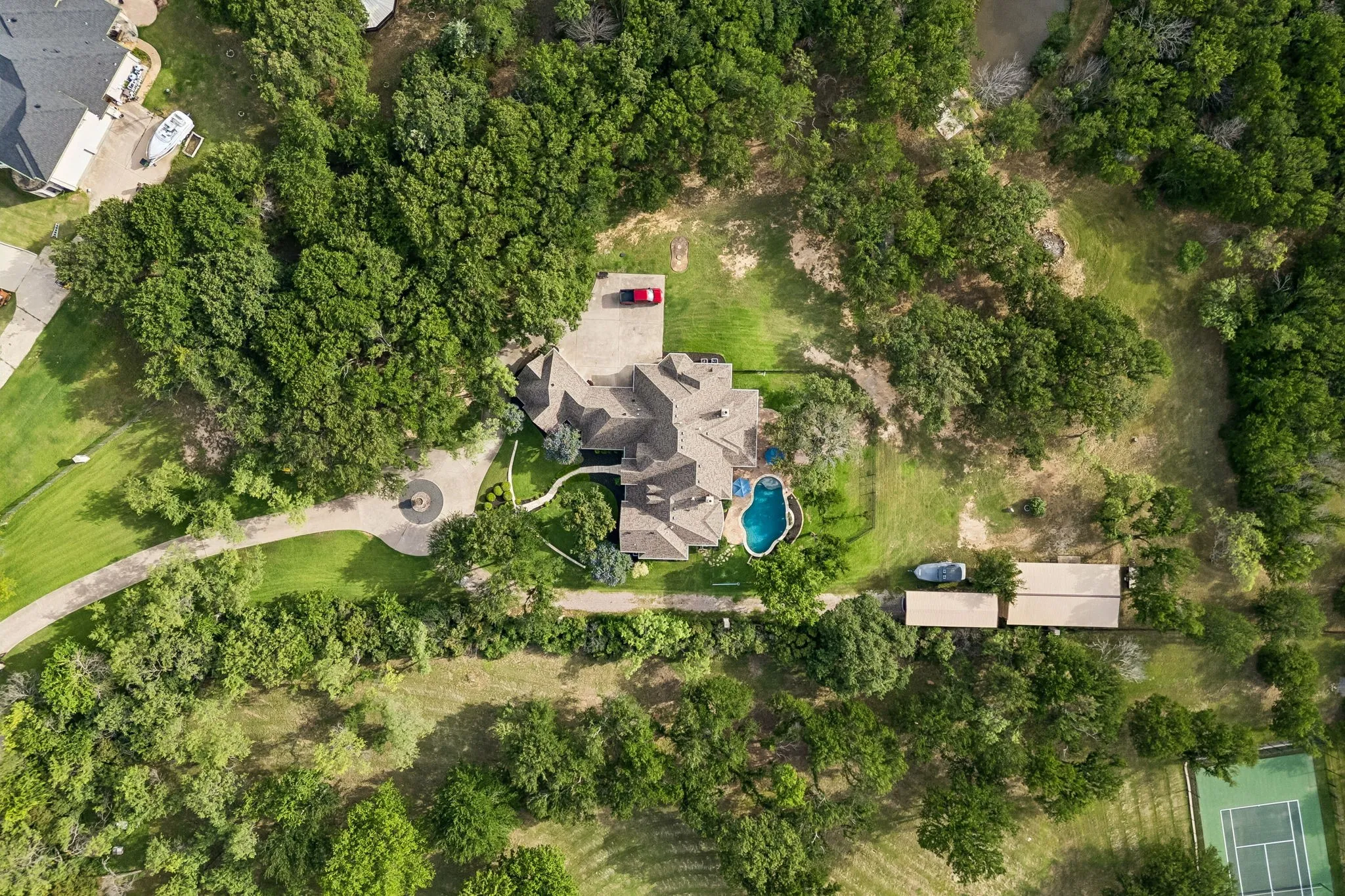 Sprawling property featuring a large residence with a multi-gabled roof, a circular driveway with a central feature, an in-ground swimming pool, and extensive surrounding treed grounds