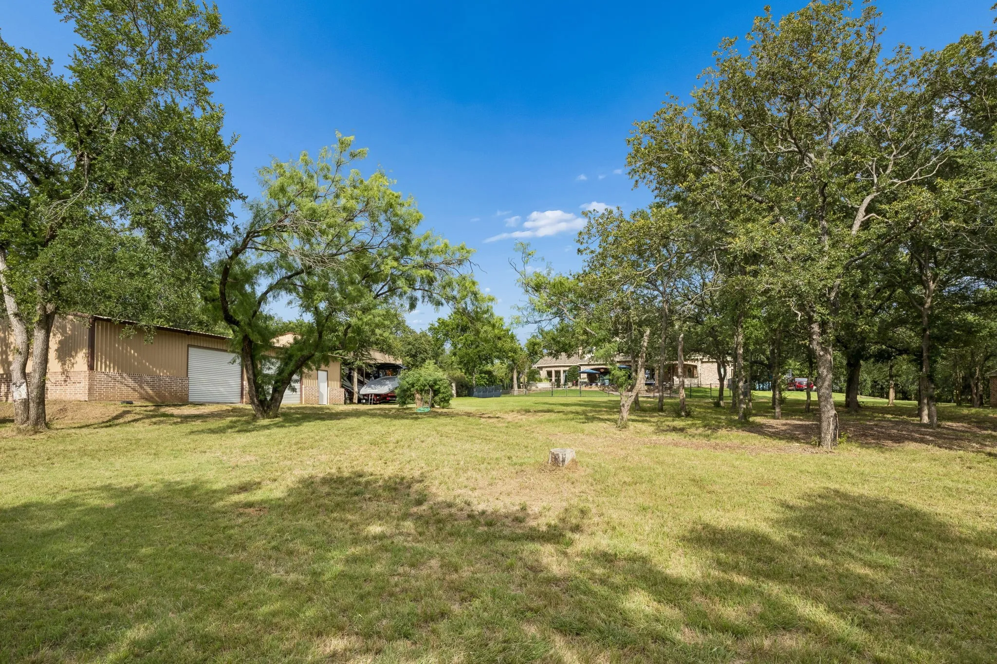 Expansive grassy acreage featuring mature trees, a metal-sided outbuilding with a garage door, and a covered structure