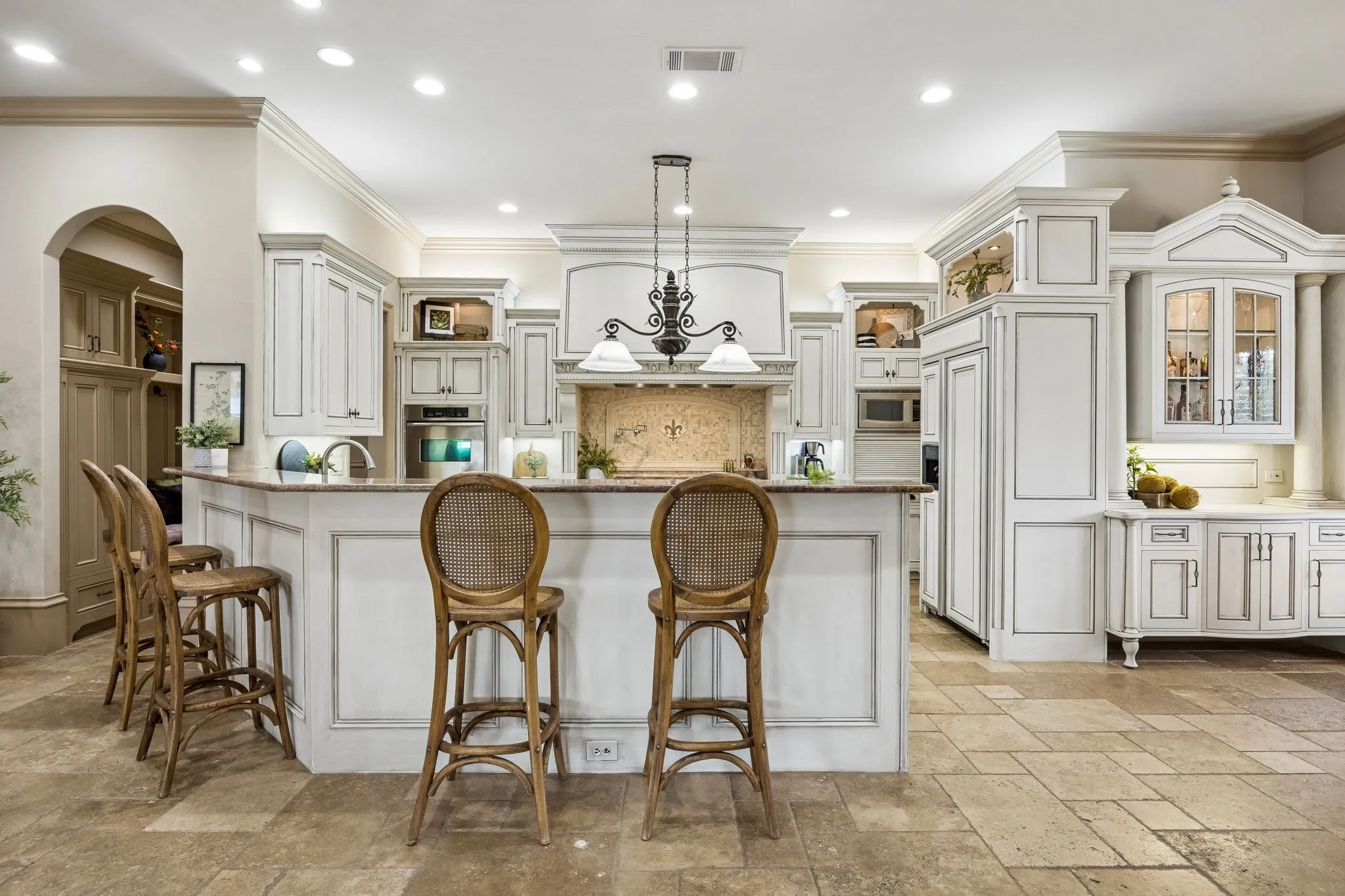 Gourmet kitchen featuring a large island with seating, built-in appliances, custom cabinetry, a decorative range hood, and tile flooring