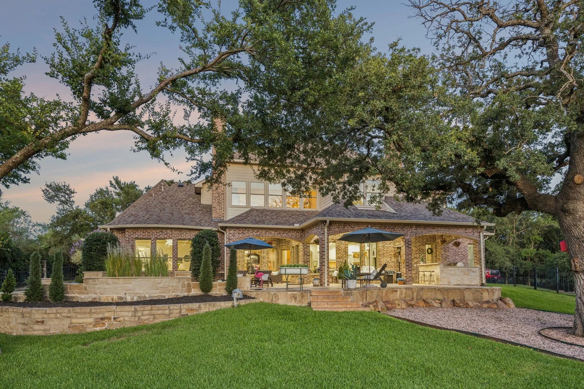 Expansive rear exterior featuring a covered patio, tiered landscaping with stone retaining walls, and a manicured lawn