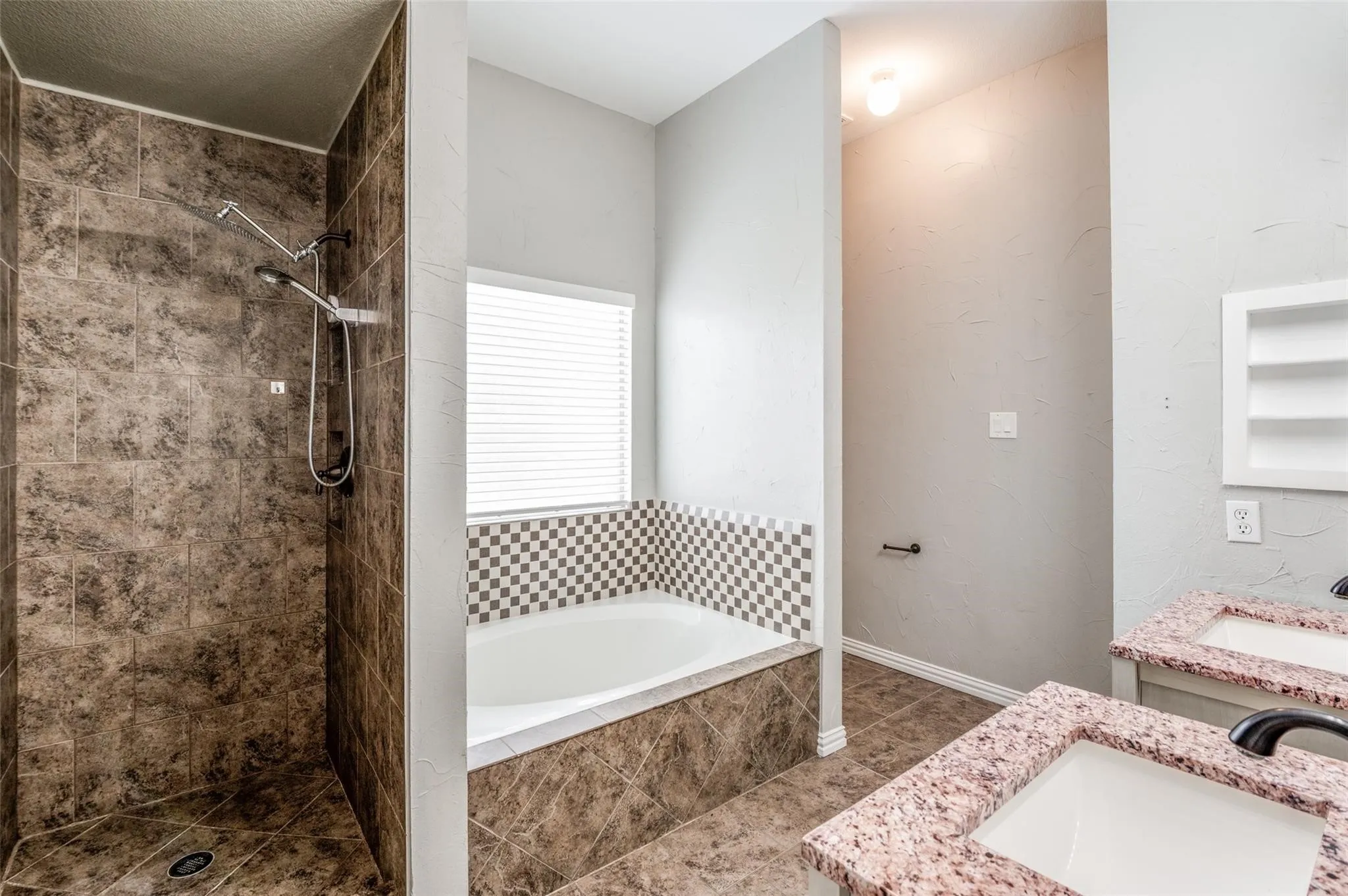 Bathroom featuring a tiled walk-in shower with dual shower heads, a built-in bathtub with a checkered tile surround, and dual vanity sinks with light-colored countertops