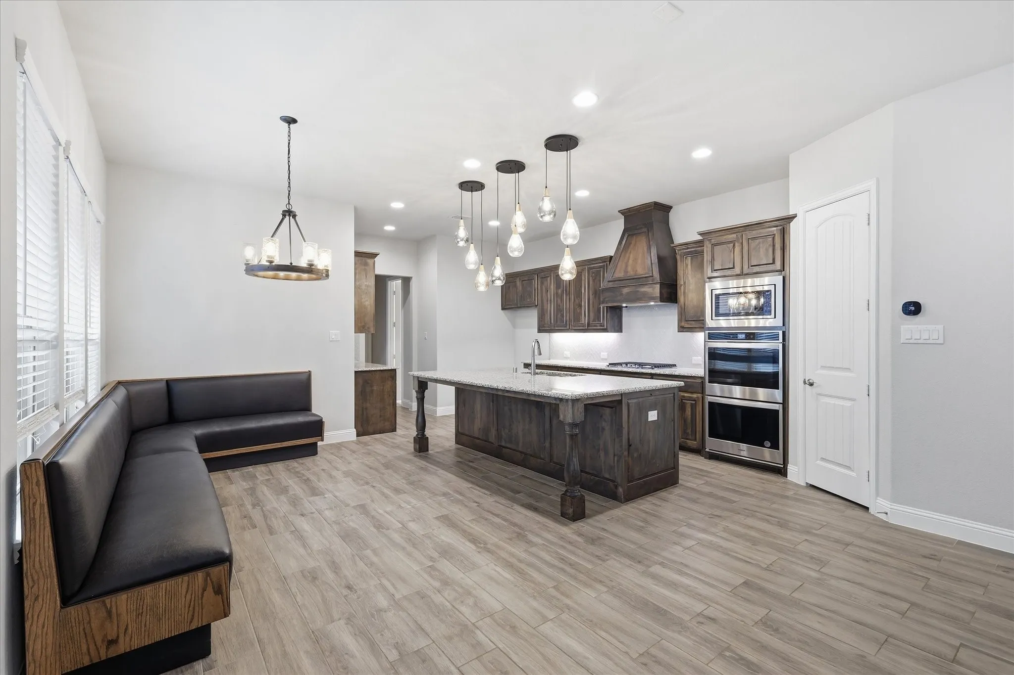 Kitchen featuring wood-finish flooring, dark wood cabinetry, a center island with pendant lighting, stainless steel double ovens, and a built-in banquette