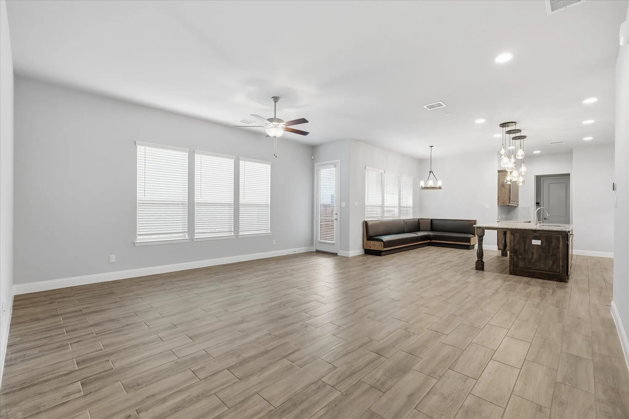 Open-concept living area featuring wood-finish tile flooring, multiple windows with blinds, recessed lighting, and a ceiling fan