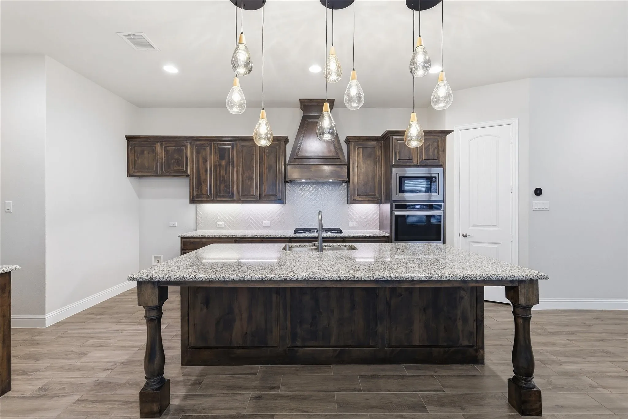 Kitchen featuring a substantial island with a speckled countertop and decorative wood legs, dark wood cabinetry, stainless steel appliances, and a tile backsplash