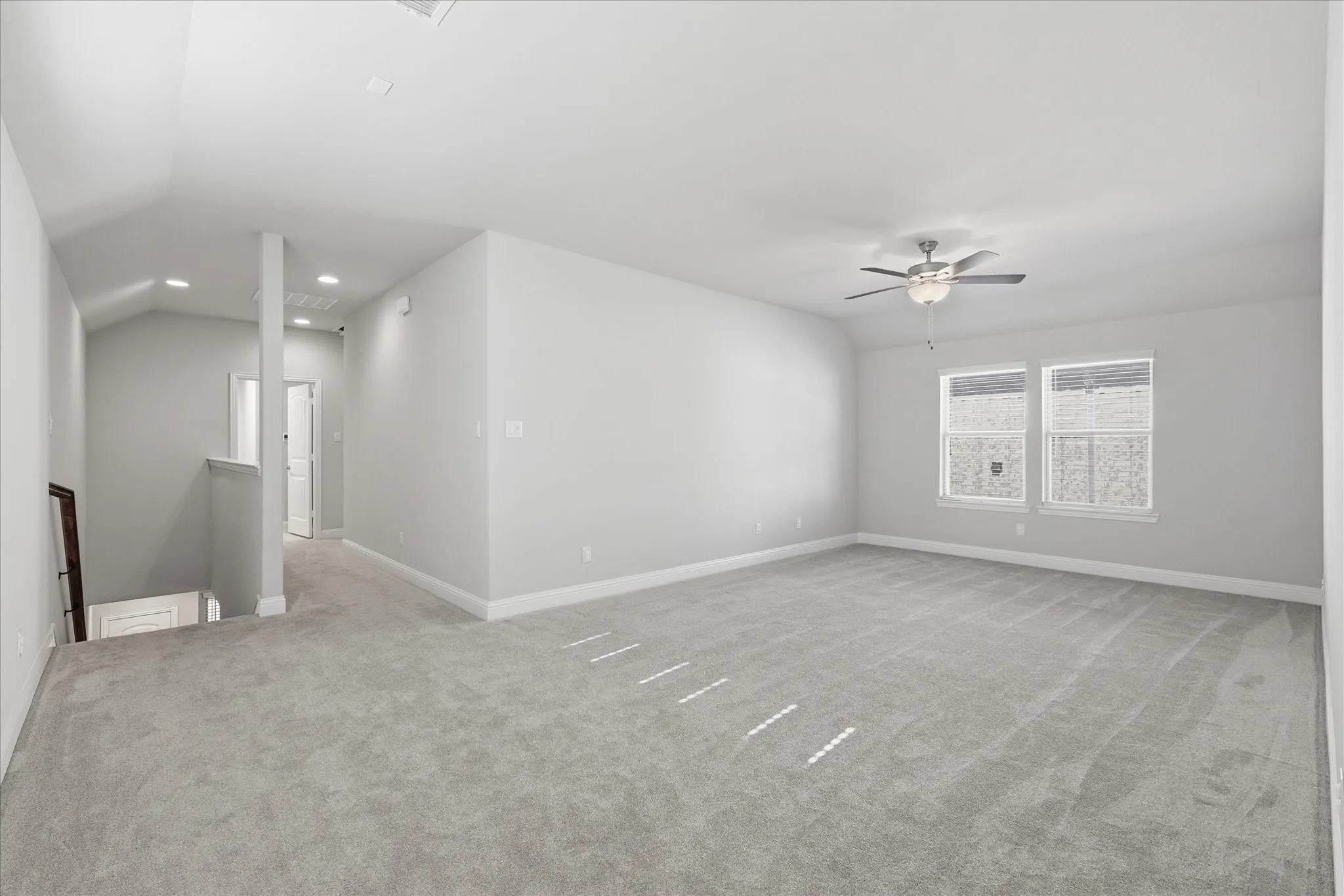 Spacious carpeted room featuring a ceiling fan with light fixture, dual windows, recessed lighting, and a partial vaulted ceiling