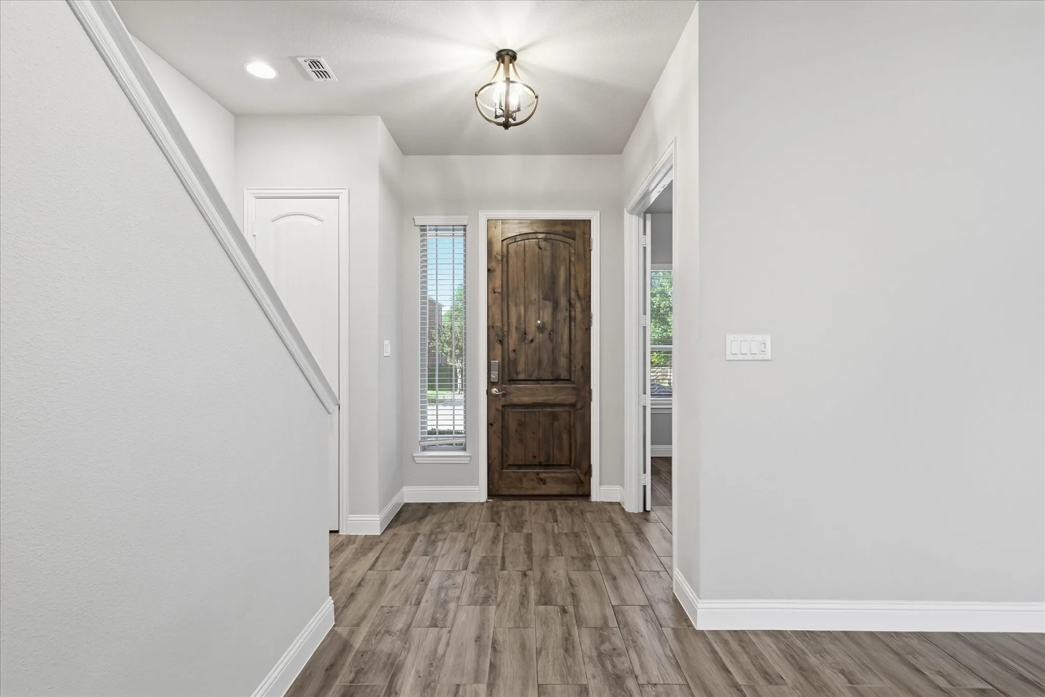 Entryway featuring a solid wood-finish door, wood-finish flooring, a contemporary ceiling light fixture, and light-colored walls