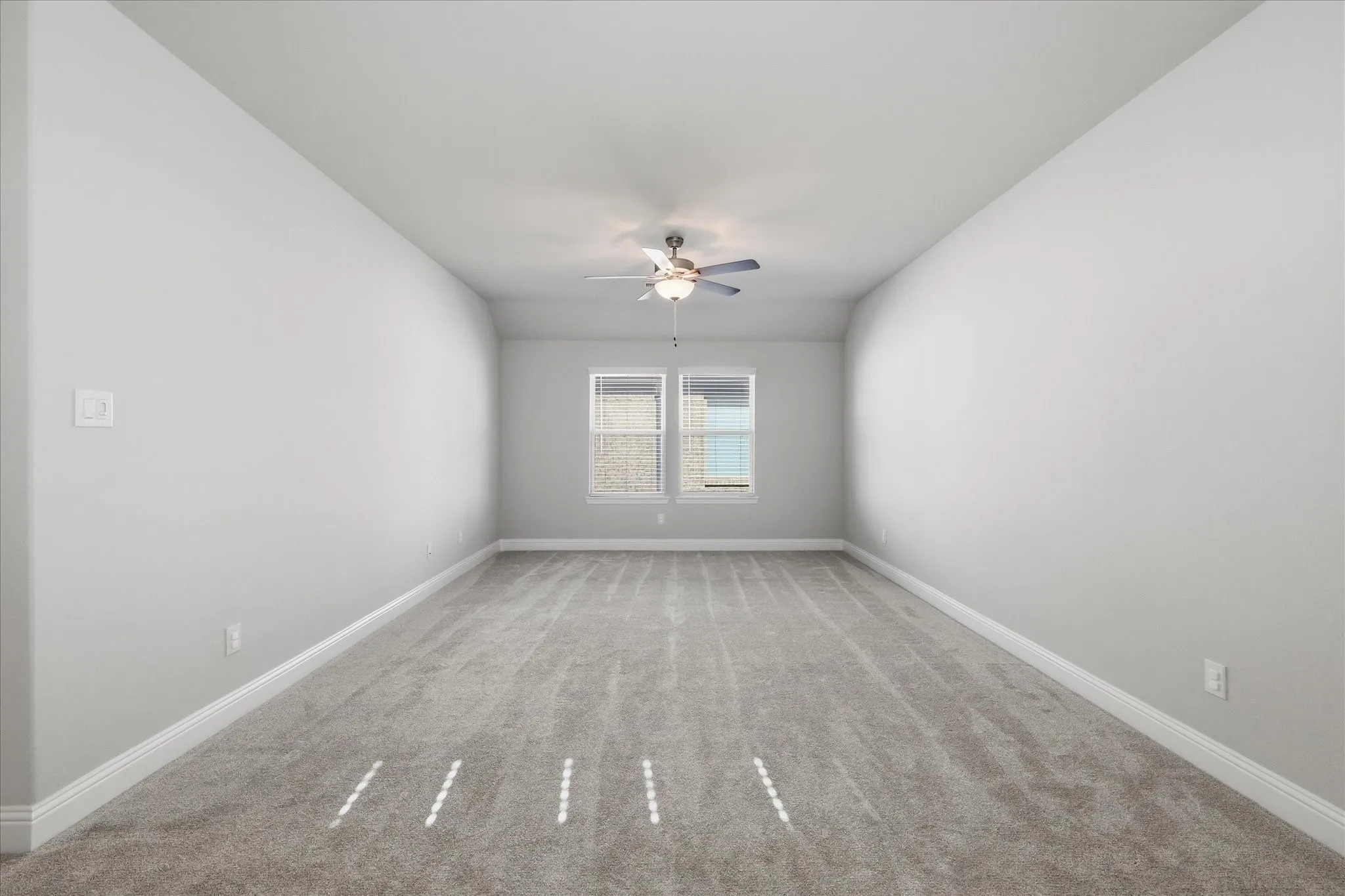 Spacious room featuring neutral carpeting, light gray walls, a ceiling fan with integrated lighting, and two windows providing natural illumination