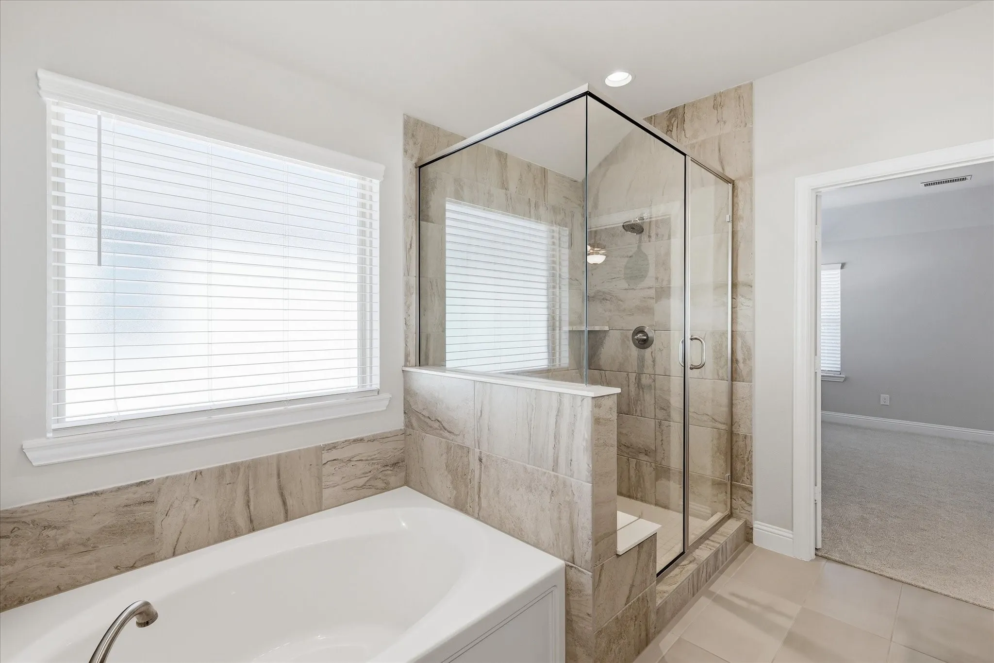 Contemporary bathroom featuring a spacious walk-in shower with clear glass enclosure and integrated shelving, a separate soaking tub, and neutral-toned wall and floor tiling