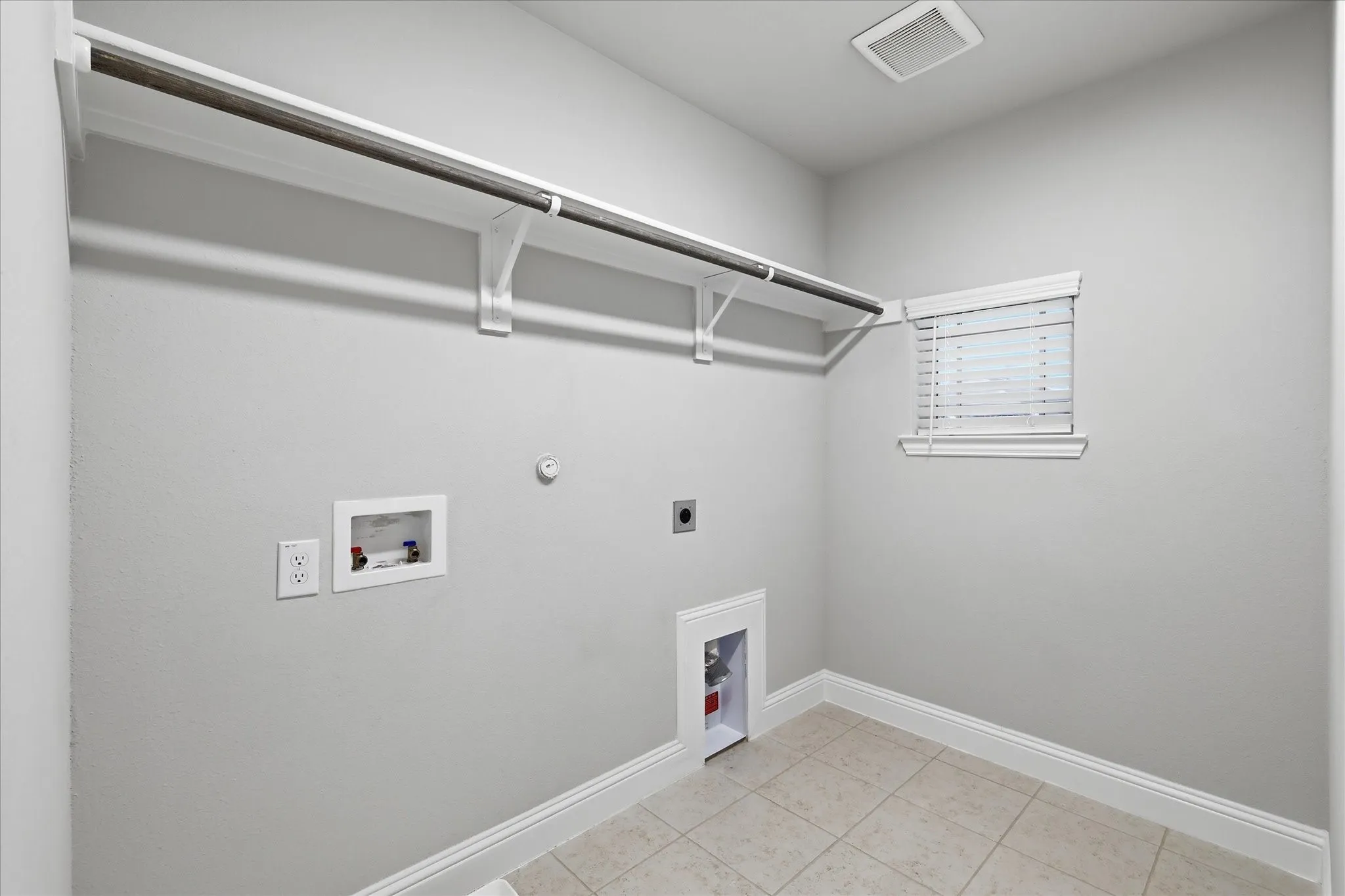 Utility space featuring tiled flooring, a window with blinds, and white baseboards