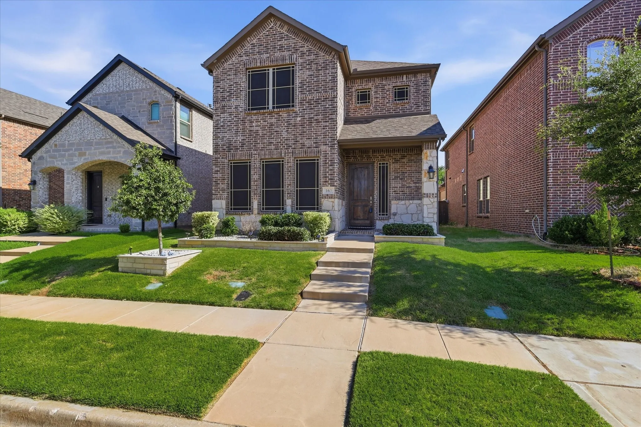 Two-story brick exterior featuring stone accents, a wood-finish front door, and a covered entry