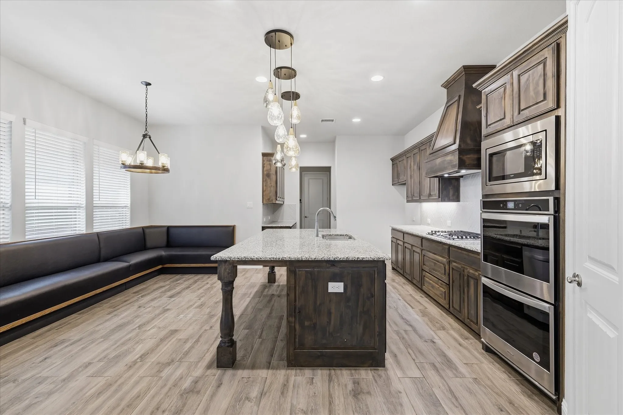Kitchen featuring wood-finish cabinetry, stainless steel appliances including a built-in microwave and double oven, a gas cooktop, and an island with a sink and stone countertop