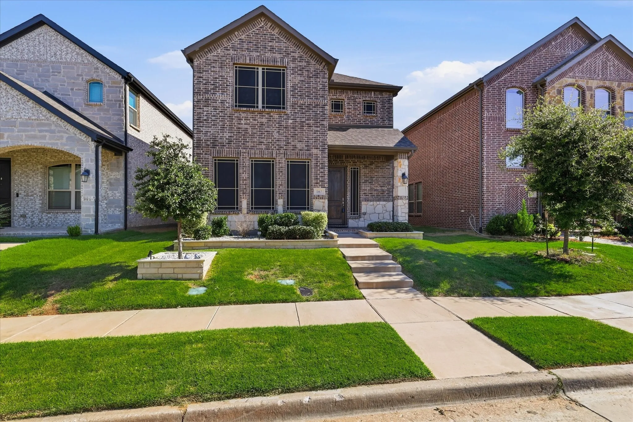 Two-story brick facade residence with stone accents, a covered front porch, and mature landscaping