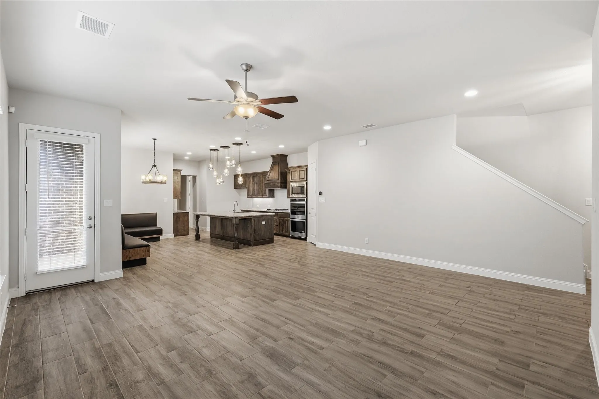 Open-concept living space featuring wood-finish tile flooring throughout, a modern kitchen with a large island and custom wood cabinetry, a built-in banquette, and recessed lighting