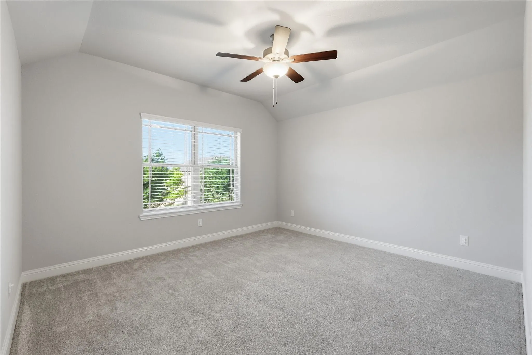 Carpeted room featuring a vaulted ceiling with a ceiling fan, a window with horizontal blinds, and neutral-toned walls