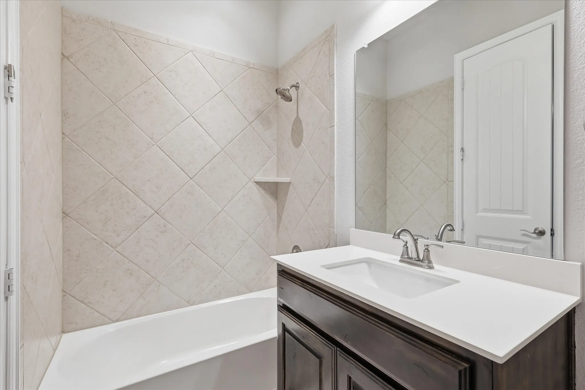Bathroom featuring a white bathtub, diamond-patterned wall tiling, dark wood-finish vanity, white countertop, and a vanity mirror