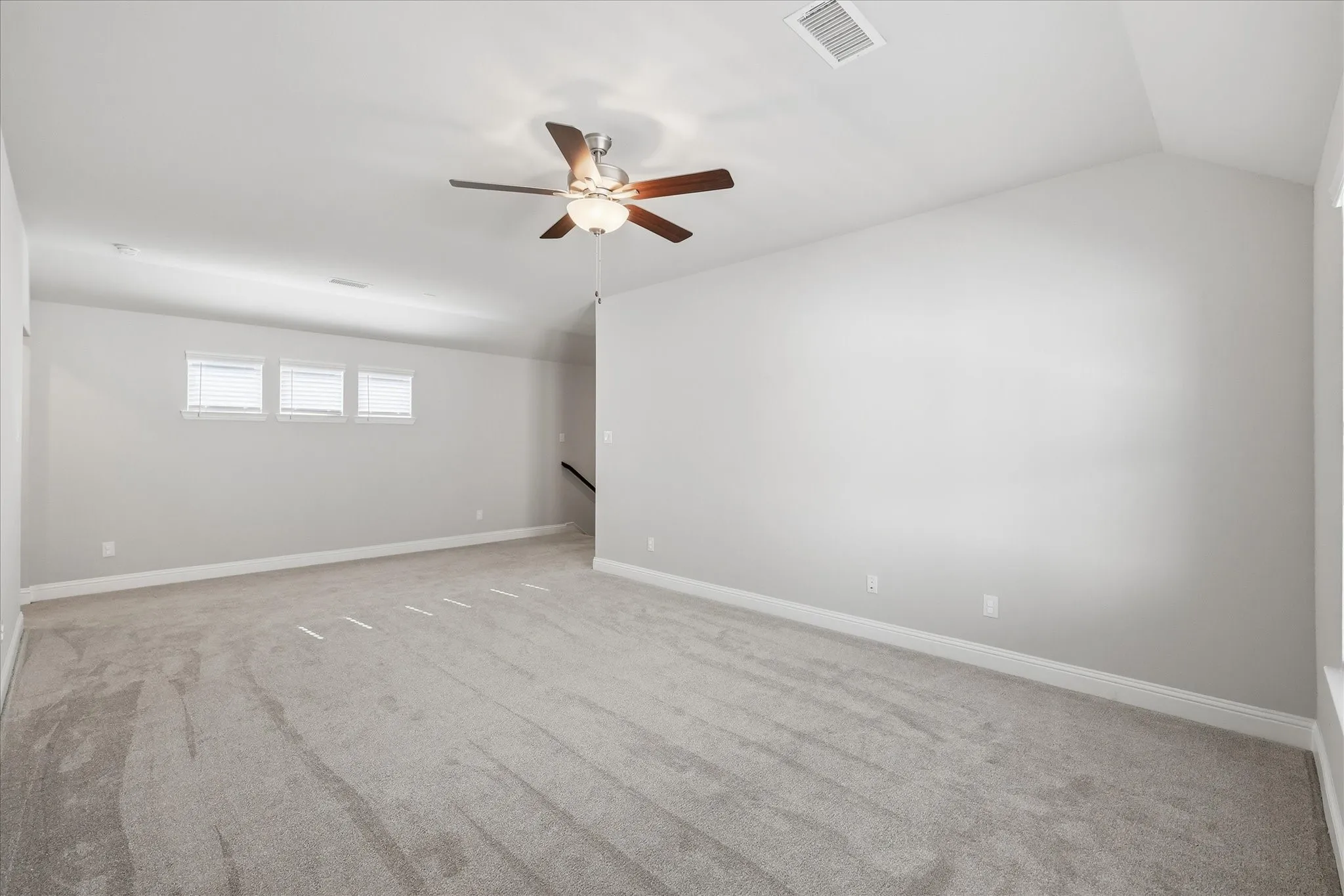 Spacious carpeted room featuring a ceiling fan with integrated lighting, multiple windows with blinds, and neutral wall tones