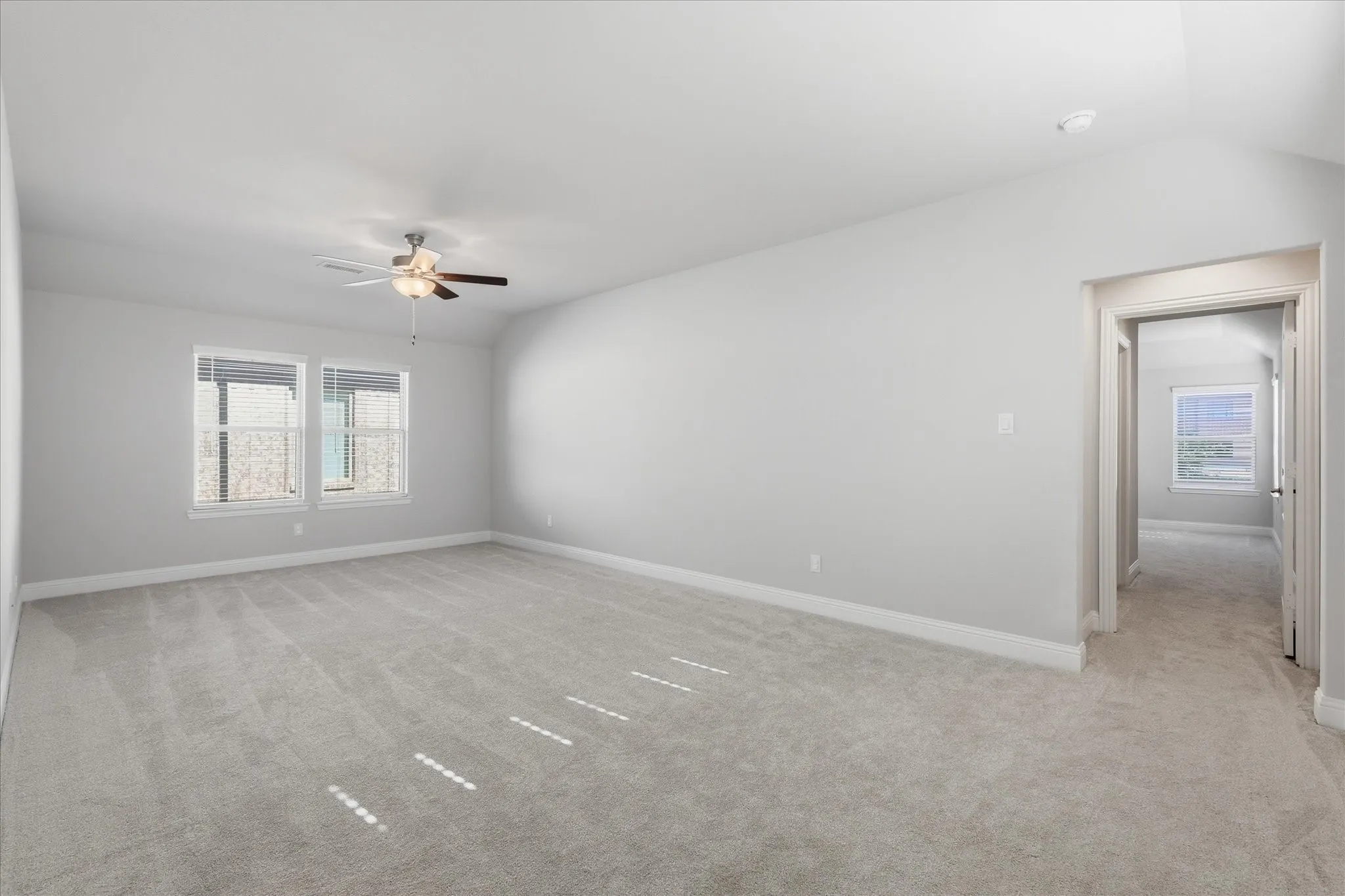 Spacious room featuring light gray carpeting, neutral wall paint, two windows with blinds, a ceiling fan with integrated lighting, and white trim