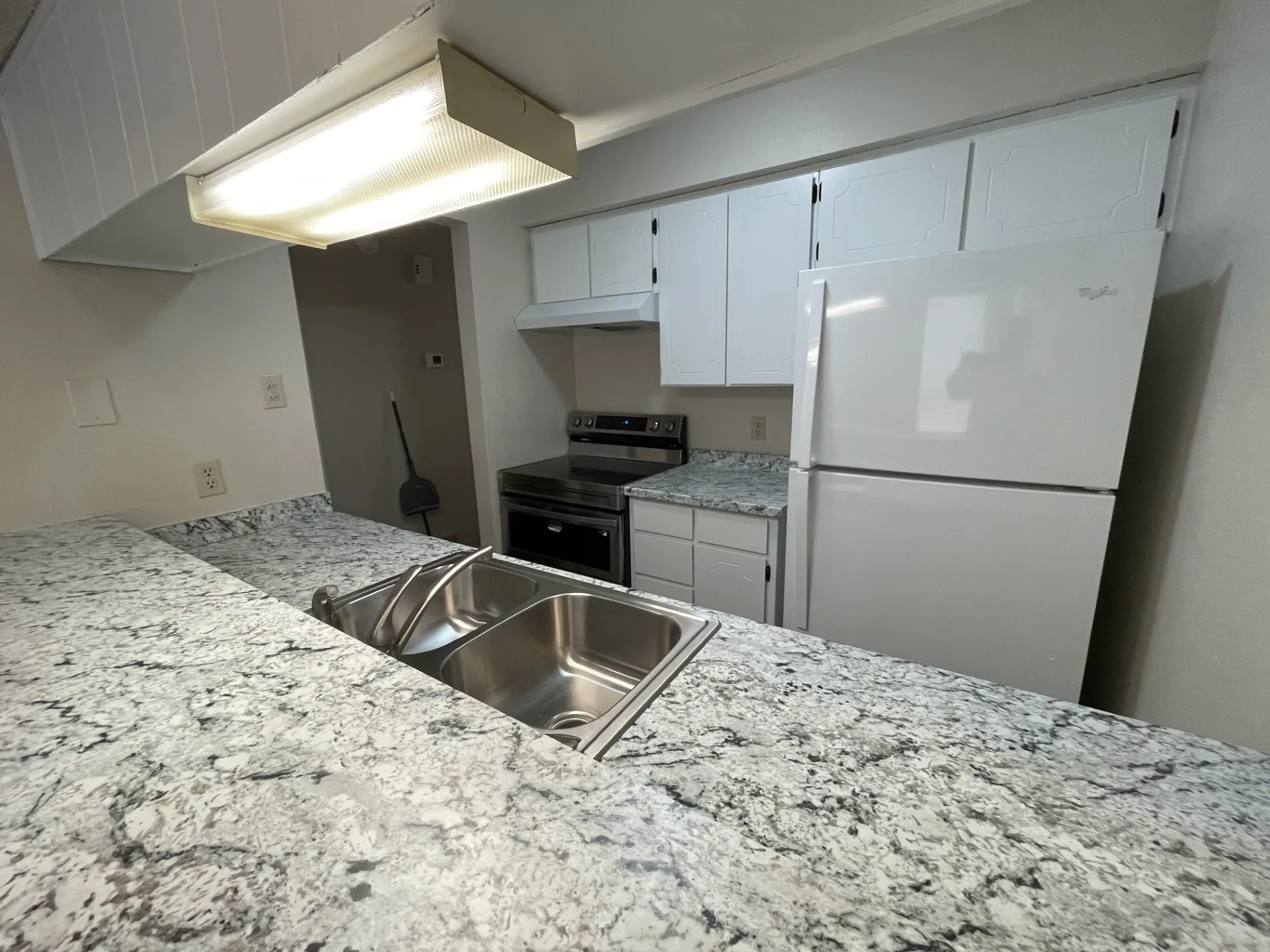 Kitchen featuring solid surface countertops, a double-basin stainless steel sink, white upper and lower cabinetry, a white refrigerator, and a stainless steel range