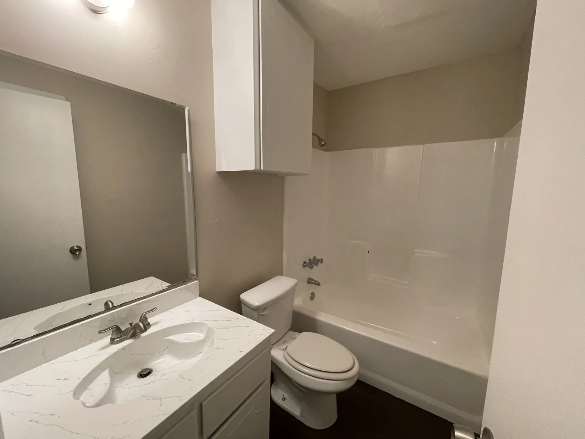 Bathroom featuring a white vanity with an integrated sink and countertop, a vanity mirror, an overhead light fixture, a toilet, a shower/tub combination, and an overhead storage cabinet