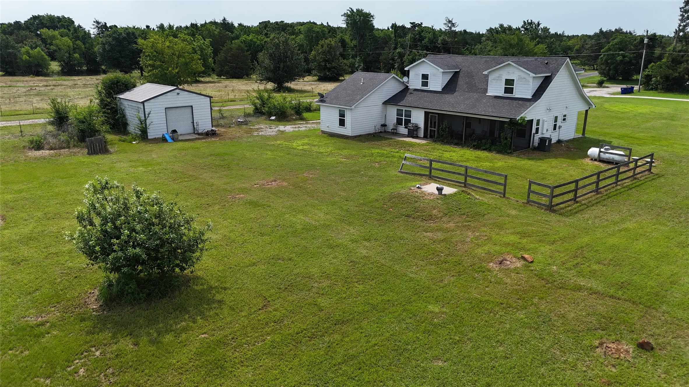 Spacious green grounds featuring a white residential structure with dormer windows, an attached screened porch, and an additional white storage shed with a metal roof