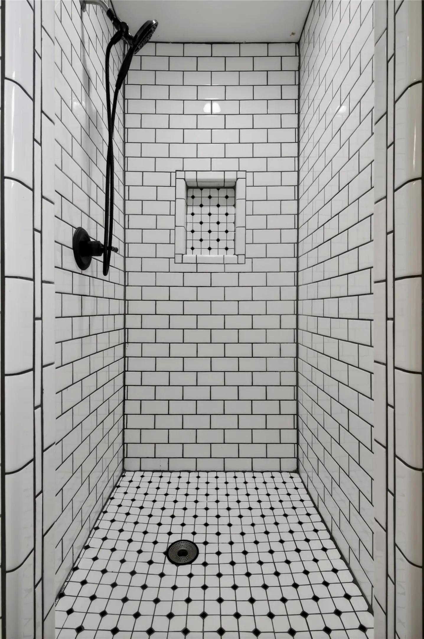 Tiled shower featuring white subway wall tiles with dark grout, a built-in shower niche with mosaic tile, and a black and white mosaic tile floor